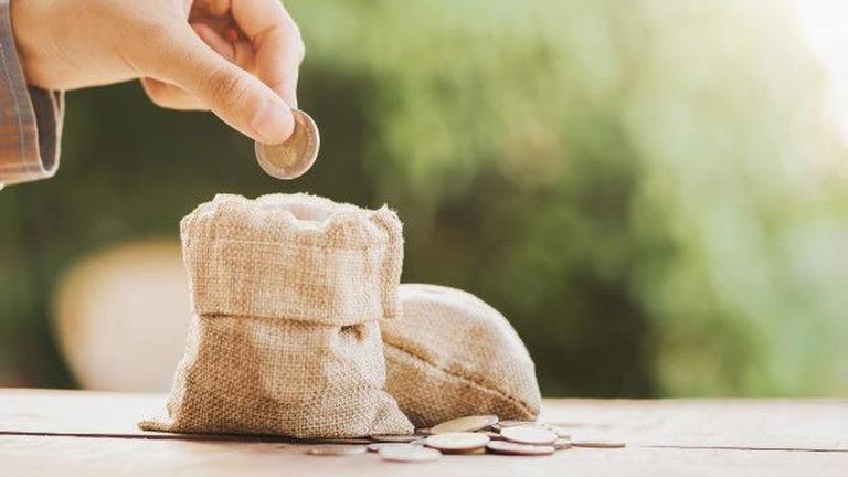 Kisah Kebaikan Khadijah Istri Nabi Muhammad  - 067346100 1588740345 Hand Puting Coins In Money Bag For Saving On Table Background - Kisah Kebaikan Khadijah Istri Nabi Muhammad